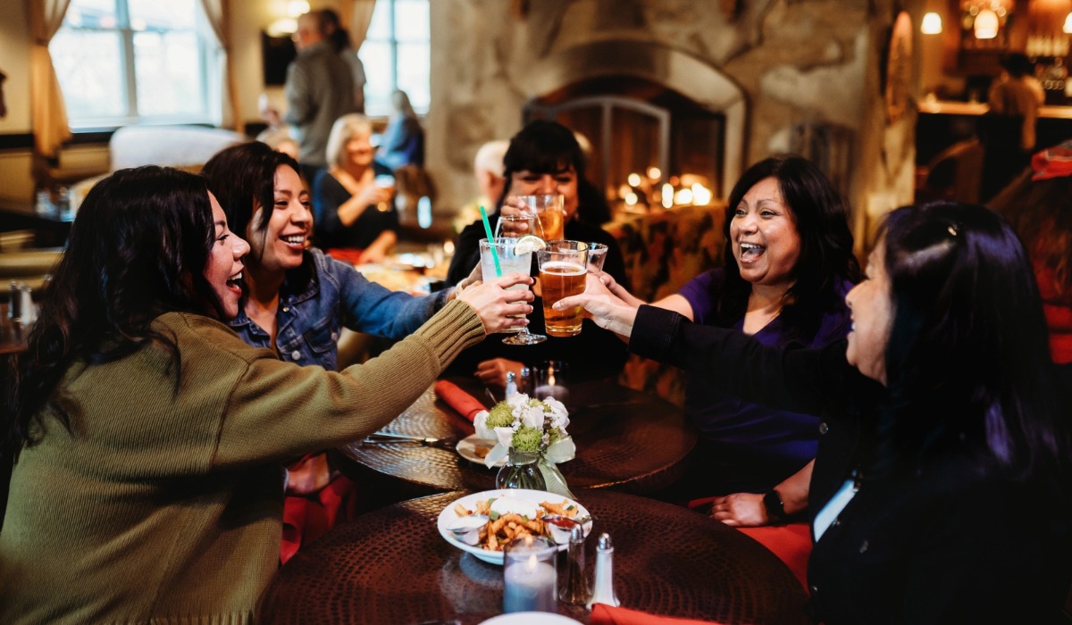 Group of women smiling, clinking drinks in front of fireplace at Fireside Lounge at the Oregon Garden Resort